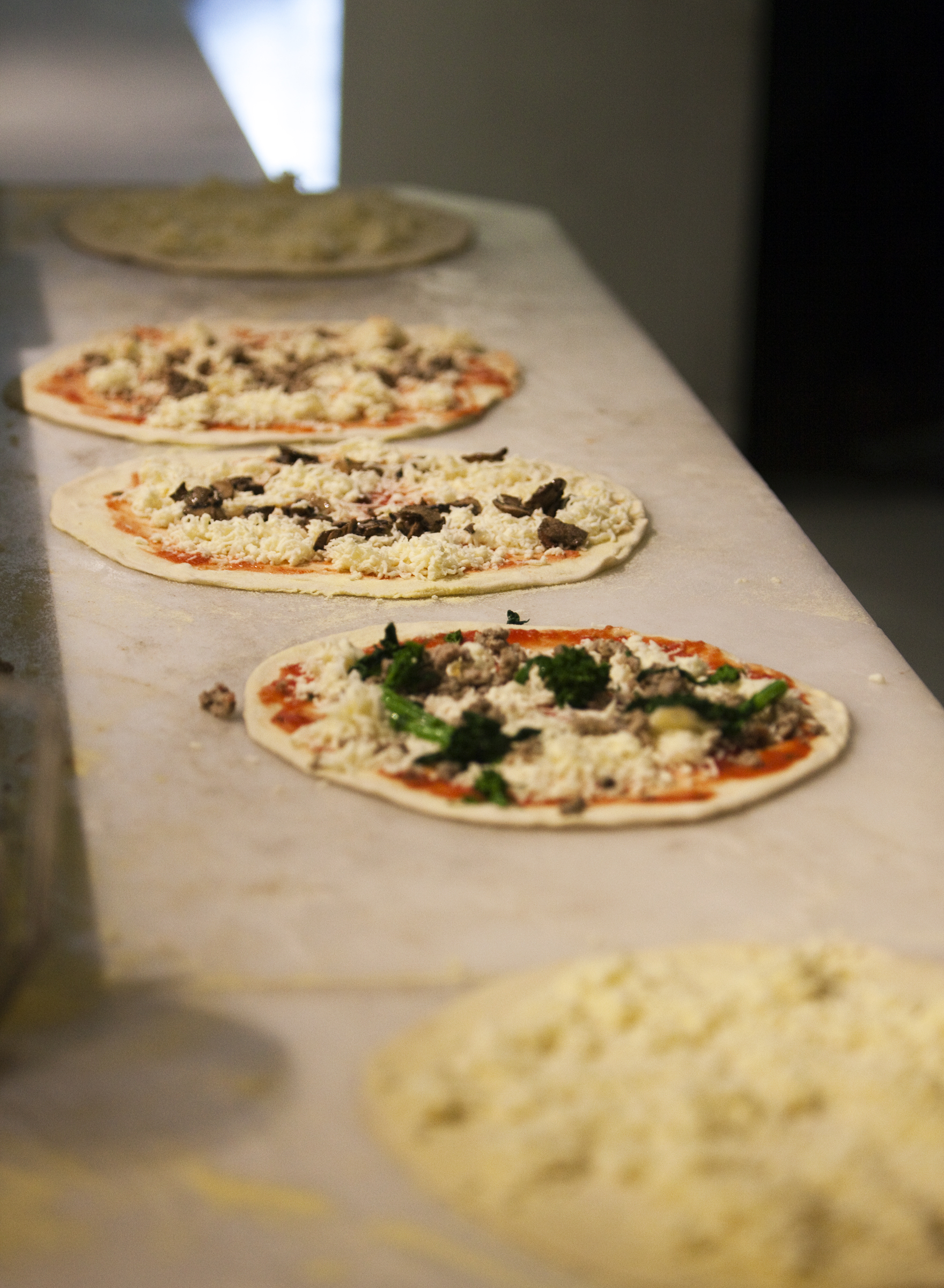 Row of hand-topped pizzas ready for the oven